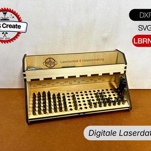 Könnte beinhalten: Ein Holz-Bit-Organizer mit verschiedenen schwarzen Bits. Der Organizer trägt die Aufschrift "SOS Create" und "Lasertechnik & Holzbearbeitung". Das Bild enthält auch den Text "DXF", "SVG" und "Digitale Laserdatei".