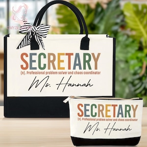May include: A canvas tote bag and a matching zippered pouch. Both items are off-white with black accents and feature the word "SECRETARY" in colorful letters, along with the text "(n). Professional problem solver and chaos coordinator" and the name "Ms. Hannah".