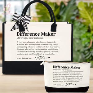 May include: A tote bag and a small pouch, both with the text "Difference Maker" in black. The tote bag has black handles and a black and white striped bow. The pouch has a black base. Both items have a definition printed on them.