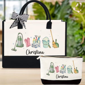 May include: A white tote bag and matching cosmetic bag with black accents. Both bags feature a cleaning supplies design, including a vacuum, gloves, and spray bottles. The name "Christina" is printed on both bags. A black and white striped bow adorns the tote bag.