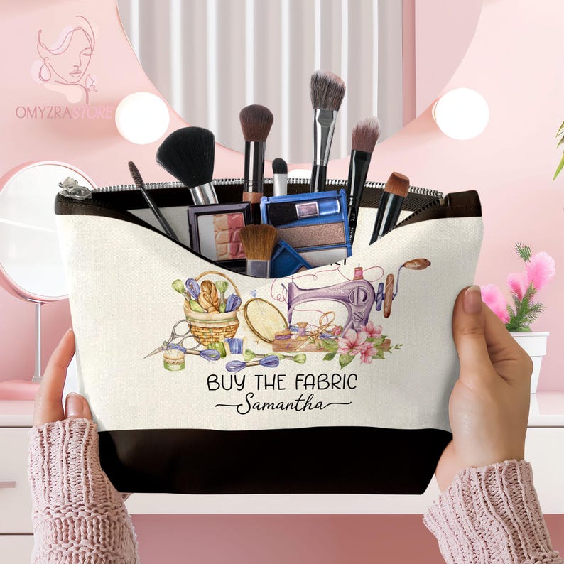 May include: A beige and black makeup bag with a zipper closure, filled with makeup brushes and products. The bag features a watercolor design of sewing notions and the text "BUY THE FABRIC Samantha".