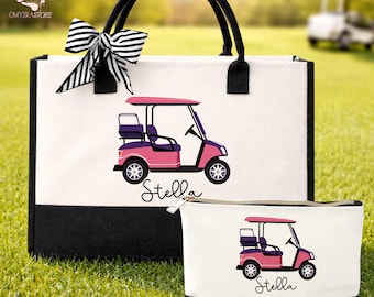 May include: A white tote bag and matching cosmetic bag with a black base and handles. Both bags feature a pink and purple golf cart design with the name "Stella" in script. A black and white striped bow adorns the tote bag.