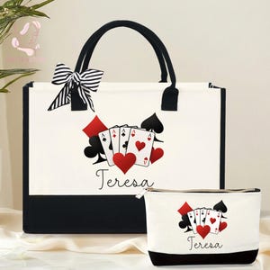 May include: A white tote bag and matching cosmetic bag with black accents. Both bags feature a playing card design with hearts, spades, clubs, and diamonds. The name "Teresa" is written in cursive below the card design. A black and white striped bow adorns the tote bag.