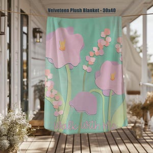 May include: A Velveteen plush blanket, 30x40 inches, featuring a floral design. The blanket has a light green background with large pink flowers and smaller pink and orange floral accents. The words "Walk With Me" are written in script.