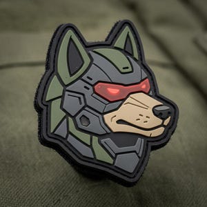 May include: A patch featuring a stylized wolf head with a robotic design. The patch has a black border, with the wolf's face in shades of gray, green, and tan. The eyes are red, and the overall design has a futuristic aesthetic.