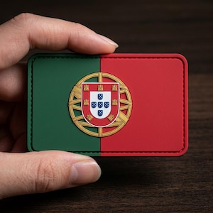 May include: A rectangular patch featuring the Portuguese flag, divided vertically into green and red sections. The Portuguese coat of arms is centered, with a gold armillary sphere and a shield displaying five blue escutcheons.