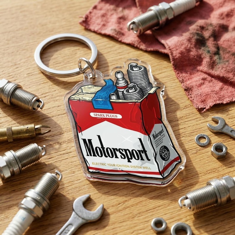 Puede incluir: Un llavero acr&iacute;lico transparente con un dise&ntilde;o rojo y blanco de "Motorsport", que se asemeja a un paquete de cigarrillos, que contiene buj&iacute;as. La imagen incluye buj&iacute;as, llaves y otras herramientas automotrices.