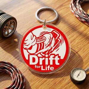 May include: A round keychain with a red and white graphic that says "Drift for Life". The keychain has a silver key ring and a clear plastic body. Other items in the image include a tire, a tire pressure gauge, and a rope.