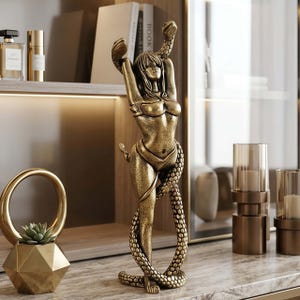 Op de afbeelding: Een bronzen sculptuur van een vrouw met een slang om haar lichaam. De vrouw heeft haar armen omhoog en de kop van de slang bevindt zich boven haar. De sculptuur is gedetailleerd en staat op een marmeren oppervlak.