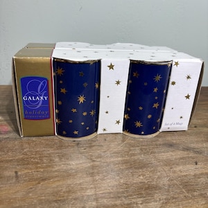 May include: A boxed set of four ceramic mugs. The mugs are navy blue with gold star patterns. The box is white with gold stars and features the words "GALAXY holiday dinnerware" on the side.