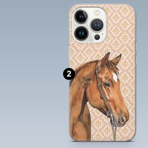 Pode incluir: Uma capa de telefone com uma pintura em aquarela de uma cabe&ccedil;a de cavalo marrom com uma mancha branca. A capa tem um fundo bege com um padr&atilde;o floral dourado repetido. As lentes da c&acirc;mera do telefone s&atilde;o vis&iacute;veis.