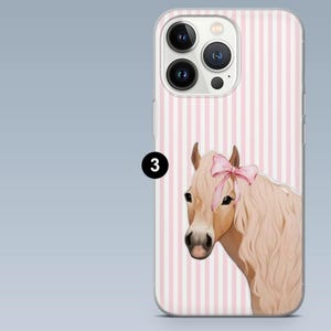 Pode incluir: Capa de telefone com fundo listrado rosa claro e branco. A capa apresenta uma ilustra&ccedil;&atilde;o de um cavalo castanho claro com um la&ccedil;o rosa. A capa do telefone tem tr&ecirc;s lentes de c&acirc;mera.