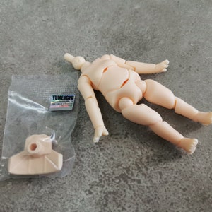 May include: A nude-colored plastic doll body with articulated joints. The doll body is lying on a gray surface. A separate nude-colored plastic doll head is also included. The head has a hole for attaching to the body. The doll parts are packaged in a clear plastic bag with a label that reads "YUMENGYU".