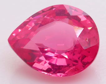 Puede incluir: Una piedra preciosa facetada en forma de pera con un color rosa intenso y saturado. La piedra presenta numerosas facetas triangulares y trapezoidales que crean una superficie compleja y reflectante, mostrando tonos rosas profundos.