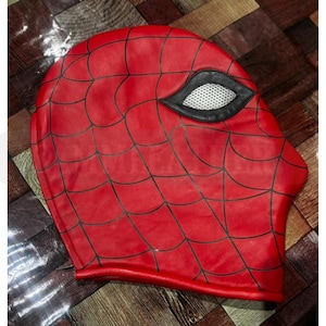 May include: A red Spider-Man mask featuring a black web design and eye openings. The eye sections are outlined in black and have a white mesh. The mask appears to be made from a smooth, possibly leather-like material.
