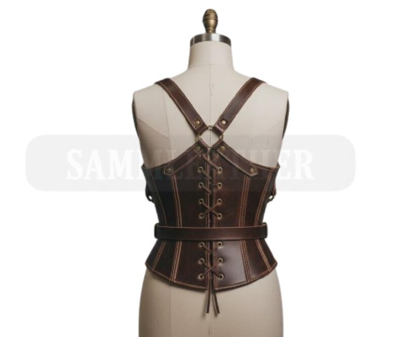 May include: Brown leather corset with adjustable straps and a laced front. The corset features a belt around the waist and decorative stitching. The straps cross in the back and attach to the corset with metal rings. The corset is displayed on a mannequin.