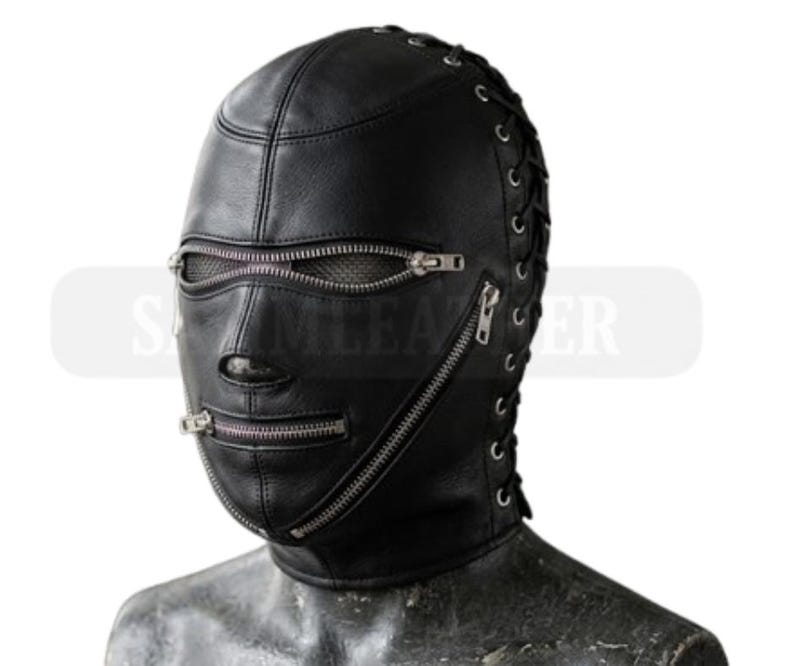 May include: Black leather hood with multiple zippers and lace-up detailing on the sides. The hood covers the entire head and face, with openings for the eyes and mouth. The zippers are silver-toned and run horizontally across the face.