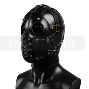May include: Black leather mask with eye and mouth openings, secured with straps and buckles. The mask features metal studs and rivets, and a lace-up closure on the lower face. The mask is designed to cover the entire head and neck.