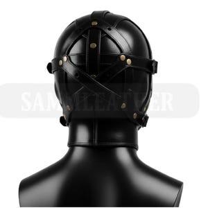 May include: Black leather hood with cross-stitched straps and brass rivets. The hood covers the entire head and neck, with a smooth, glossy finish. The product is displayed on a black mannequin head.