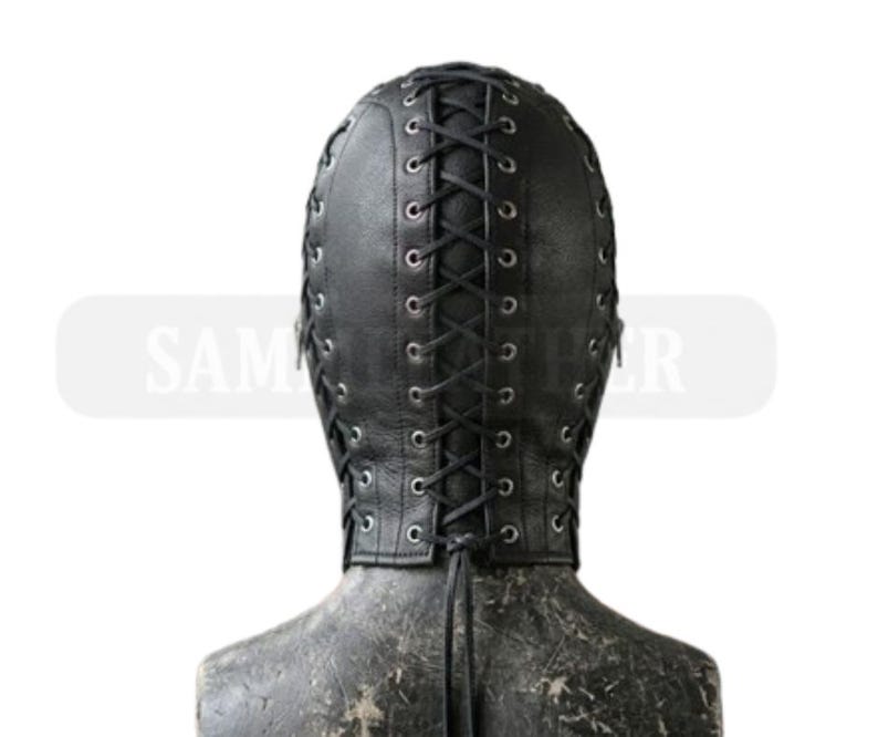 May include: Black leather hood with a lace-up design. The hood covers the entire head and neck, with eye and mouth openings. The back of the hood features a vertical lace-up closure. The hood is on a mannequin.