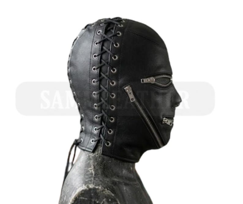 May include: A black leather hood with a full face design. The hood features a lace-up back and two zippers across the face. The hood is designed to cover the entire head and neck.