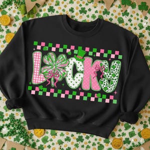 May include: Black sweatshirt with the word "LUCKY" in a colorful design. The letters are decorated with pink polka dots, green shamrocks, and a green leprechaun hat. The word is framed by a pink and green checkered pattern, perfect for St. Patrick's Day.