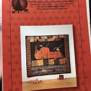 May include: A printed pattern sheet from Patchwork Moon Designs featuring a square quilt with orange pumpkins on a dark grid background, surrounded by a plaid border. The sheet includes contact information and a logo with a tree and deer silhouette.