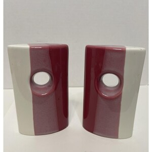 May include: A pair of ceramic bookends, each featuring a vertical design with a white stripe on one side and a burgundy stripe on the other. A circular hole is centered on each bookend.