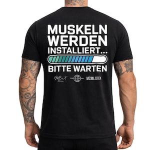 Könnte beinhalten: Schwarzes T-Shirt mit weißem Text: "MUSKELN WERDEN INSTALLIERT... BITTE WARTEN" über einer Ladebalken-Grafik. Das Shirt zeigt auch die Logos "StB.X" und "WORLD WEAR" sowie die römische Zahl "MCMLXXX".