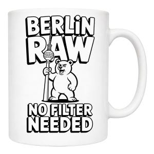 Pu&ograve; includere: Tazza in ceramica bianca con un design in bianco e nero. Il disegno presenta la scritta "BERLIN RAW" sopra un orso dei cartoni animati che tiene una torre, con "NO FILTER NEEDED" sotto. La tazza ha un manico curvo.