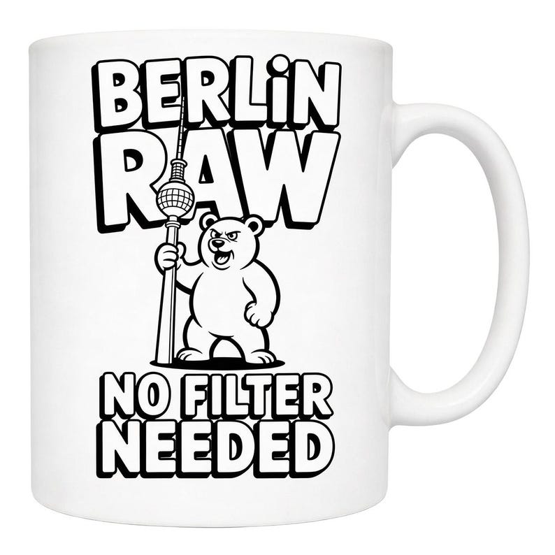 Pu&ograve; includere: Tazza in ceramica bianca con un design in bianco e nero. Il disegno presenta la scritta "BERLIN RAW" sopra un orso dei cartoni animati che tiene una torre, con "NO FILTER NEEDED" sotto. La tazza ha un manico curvo.