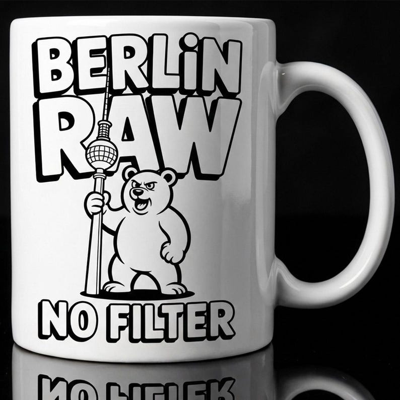 Pu&ograve; includere: Tazza in ceramica bianca con la scritta "BERLIN RAW NO FILTER" in lettere nere. Un orso dei cartoni animati che tiene una struttura alta &egrave; al centro. La tazza ha un manico curvo.