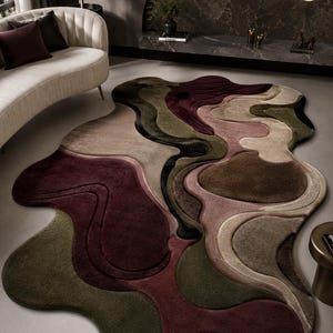 May include: An area rug with an irregular, organic shape featuring a layered, multi-dimensional design. The surface displays a palette of deep burgundy, olive green, taupe, and black, with carved, flowing lines that create a textured, topographical effect.