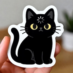 May include: A black cat sticker with a white border. The cat has yellow eyes, whiskers, and a starburst design on its forehead. The cat is sitting with its tail curled.