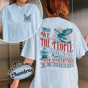 Puede incluir: Camiseta azul claro con un diseño patriótico. La parte delantera presenta un emblema de águila y el texto "1776-2026". La parte trasera muestra una bandera estadounidense, un águila, un barco y las palabras "We The People" y "250th Anniversary of the United States".