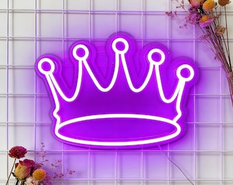 May include: A purple neon crown sign with a white outline, mounted on a white grid background. The crown has five points, each topped with a small circle. Dried flowers in shades of yellow and red are arranged on either side of the sign.