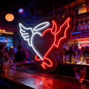May include: A neon sign in a bar features a heart shape with angel wings and a devil's tail. The sign is outlined in white and red neon lights. The bar has a wooden counter and is dimly lit with a red and blue color scheme.