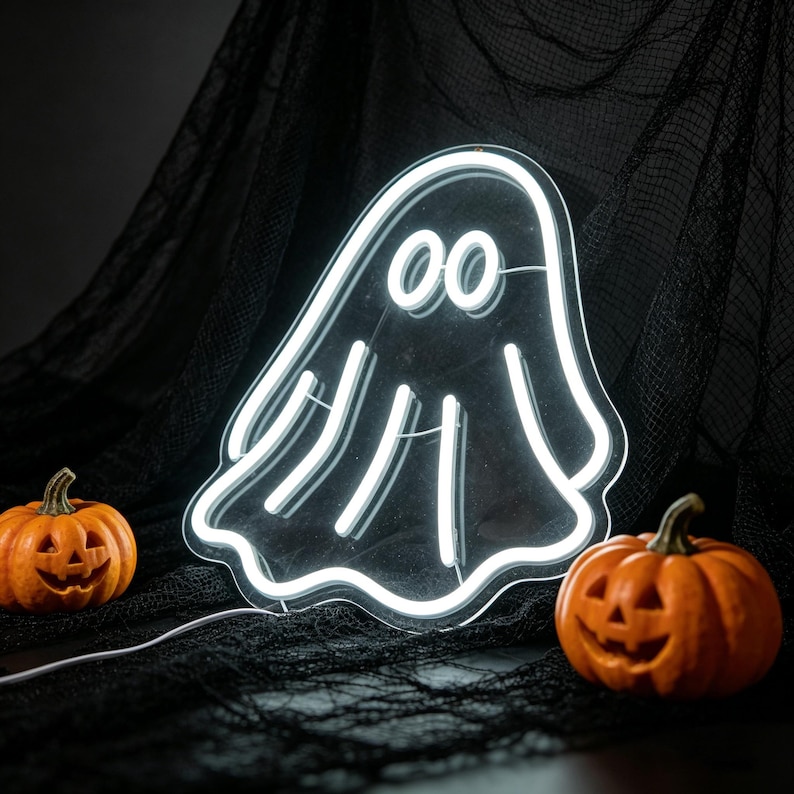 May include: A white neon ghost sign with two carved orange pumpkins on either side. The ghost has two round eyes and a wavy outline. The pumpkins have carved faces. The background is black.