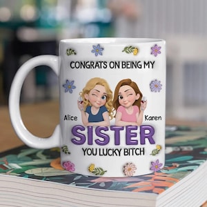 May include: White ceramic mug with a handle, featuring a graphic of two cartoon women, flowers, and the text "CONGRATS ON BEING MY SISTER YOU LUCKY BITCH". The mug has the names "Alice" and "Karen" printed on it.