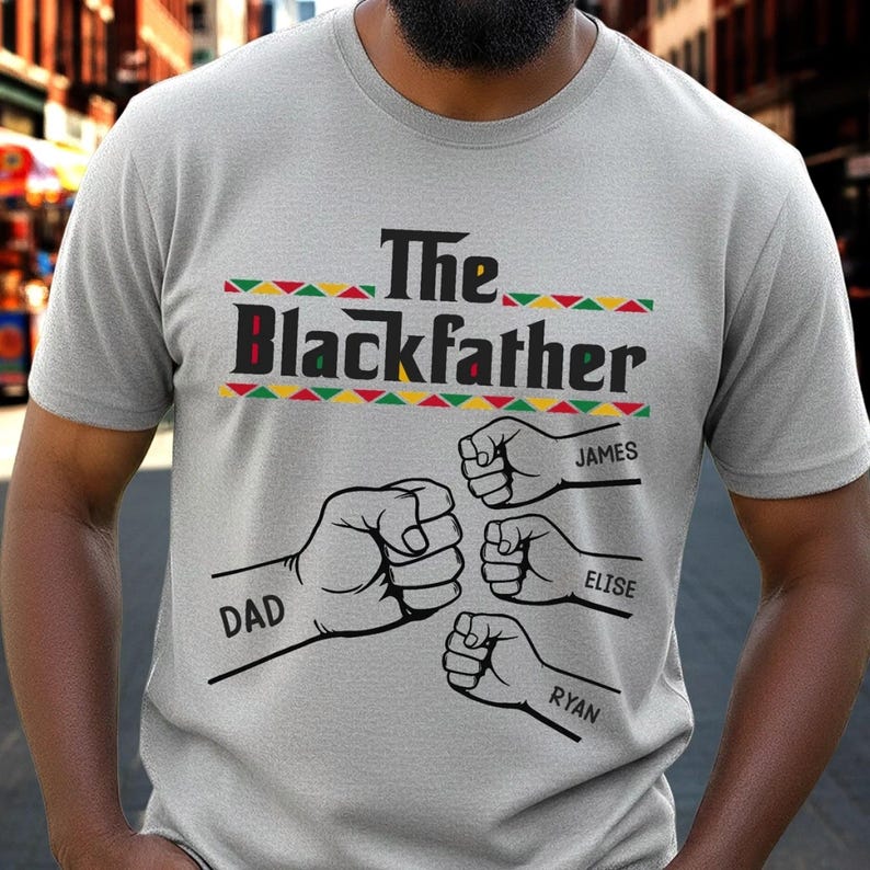 May include: A light gray t-shirt with the text "The Blackfather" in black and red, with a decorative border of green, yellow, and red triangles. Below the text are four fists with the names "DAD", "JAMES", "ELISE", and "RYAN".