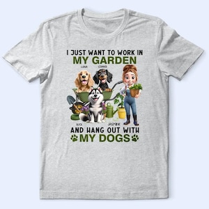 May include: Light gray t-shirt featuring a graphic of a woman gardening with four dogs in a wheelbarrow. Text reads "I just want to work in my garden and hang out with my dogs."