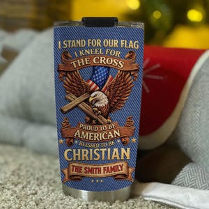 May include: A stainless steel tumbler with a blue denim-like background. The tumbler features an American flag, an eagle, and the text "I STAND FOR OUR FLAG, I KNEEL FOR THE CROSS, PROUD TO BE AMERICAN, BLESSED TO BE CHRISTIAN, THE SMITH FAMILY."