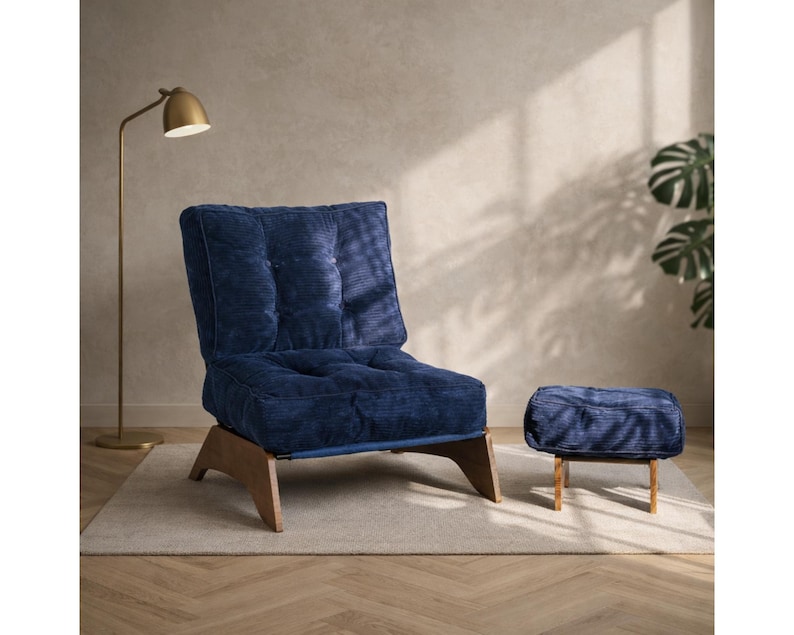 May include: A navy blue corduroy armchair and matching ottoman with wooden legs. The chair has a tufted back and seat. A gold floor lamp is in the background, and the furniture sits on a neutral-colored rug.