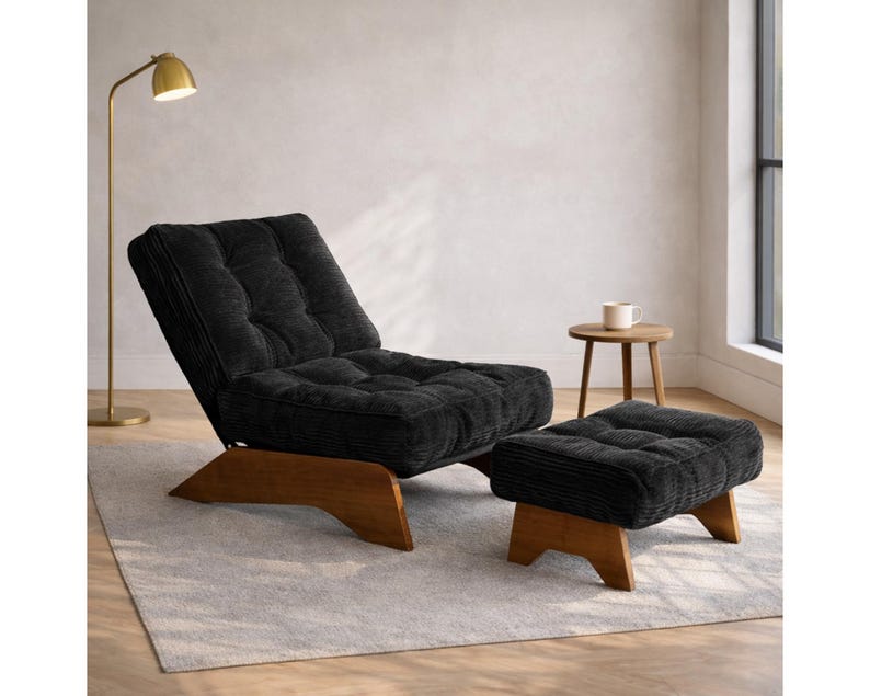 May include: A black corduroy lounge chair and matching ottoman set. The chair has a tufted back and seat, with a wooden base. The ottoman is square and also has a wooden base. A gold floor lamp and small wooden side table are also in the room.