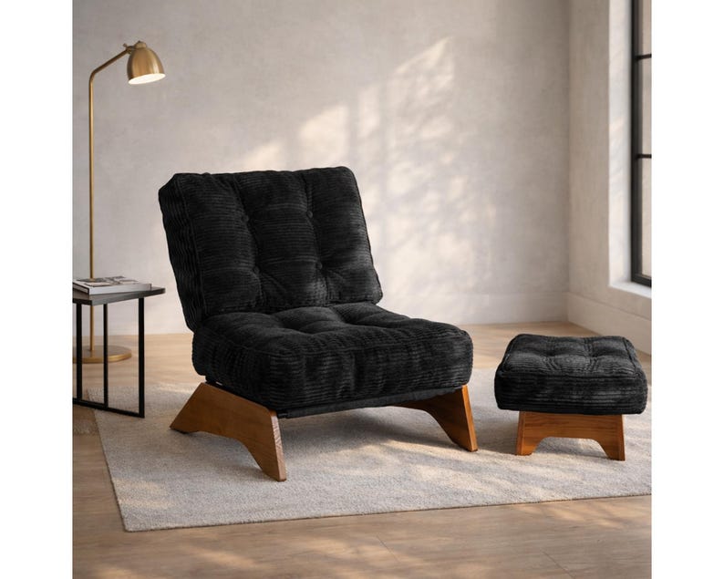 May include: Black corduroy armchair and matching ottoman with wooden legs. The chair has a tufted back and seat. The ottoman is square and also has a tufted top. The chair and ottoman are on a light-colored rug.