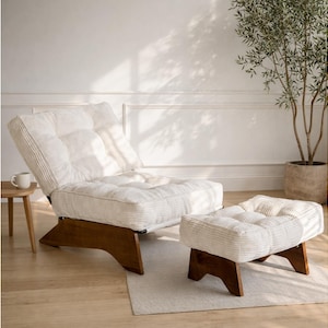 May include: A cream-colored, tufted lounge chair and matching ottoman with a wooden base. The chair is angled back, and the ottoman is positioned in front. The set is on a light-colored rug, with a small side table and a potted plant in the background.