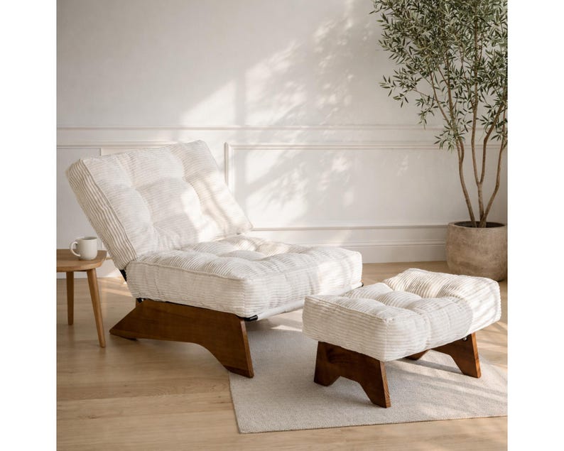 May include: A cream-colored, tufted lounge chair and matching ottoman with a wooden base. The chair is angled back, and the ottoman is positioned in front. The set is on a light-colored rug, with a small side table and a potted plant in the background.