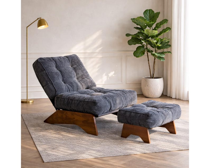 May include: A modern, corduroy upholstered chair and ottoman set in a muted blue-gray hue. The chair features a reclining back and sits on a wooden base. The ottoman mirrors the chair's design. A gold floor lamp and potted plant are in the background.