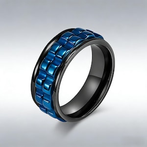 Puede incluir: Un anillo negro y azul con una banda texturizada y giratoria. El anillo presenta una banda negra brillante con una sección central azul vibrante y texturizada. El diseño es moderno y llamativo, adecuado para el uso diario.
