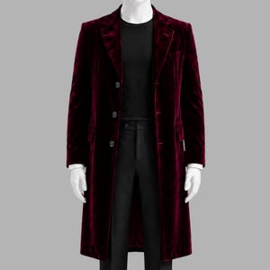 Peut inclure: Un long manteau en velours bordeaux avec une fermeture à trois boutons. Le manteau présente un revers cranté et une coupe ajustée. Le manteau est présenté sur un mannequin, mettant en valeur son design élégant et sa texture luxueuse. Il est associé à un pantalon noir et un haut noir.